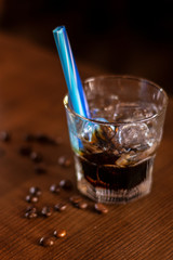 khalua drink with ice in glass with blue straw and coffee beans on wooden table