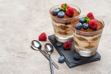 Classic tiramisu dessert with blueberries and raspberries in a glass on stone serving board on concrete background