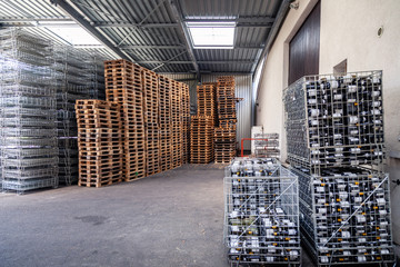Large warehouse at the factory, winery, bottles of wine in metal baskets ready for transportation, piles of wooden pallets. Concept importer wine, merchant