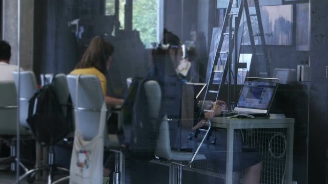 Two young girl - office workers, sitting at table, work at a computer in a modern office building