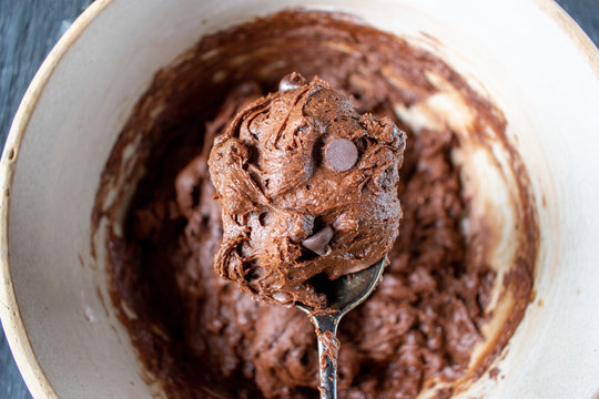 spoon of chocolate chip cookie dough batter over mixing bowl flat lay