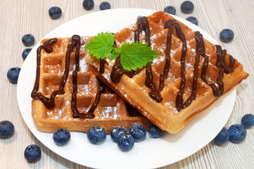 Belgian waffles on a plate with chocolate sauce and blueberries