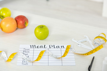meal plan, measure tape, caliper, pen and fresh fruits on wooden surface
