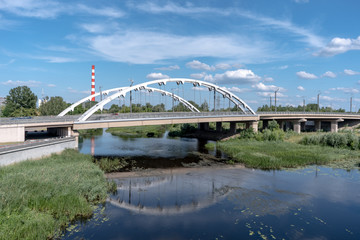 Big steel bridge over the river against blue cloudy sky in Brest, Belarus, on the summer day. Architecture and nature in one picturesque lanscape