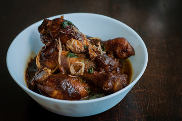 Malaysian dish of Ayam Masak Kicap or deep fried chicken in black soy gravy in a white bowl.