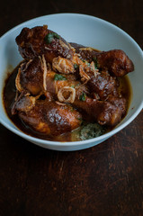 Malaysian dish of Ayam Masak Kicap or deep fried chicken in black soy gravy in a white bowl.