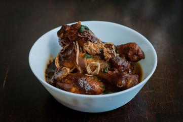 Malaysian dish of Ayam Masak Kicap or deep fried chicken in black soy gravy in a white bowl.