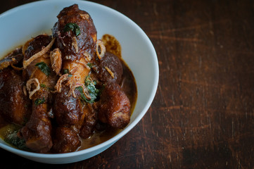 Malaysian dish of Ayam Masak Kicap or deep fried chicken in black soy gravy in a white bowl.
