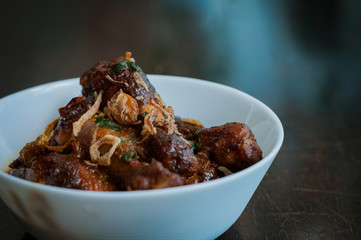 Malaysian dish of Ayam Masak Kicap or deep fried chicken in black soy gravy in a white bowl.
