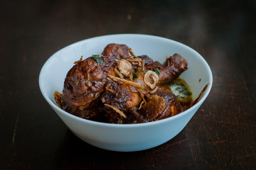 Malaysian dish of Ayam Masak Kicap or deep fried chicken in black soy gravy in a white bowl.