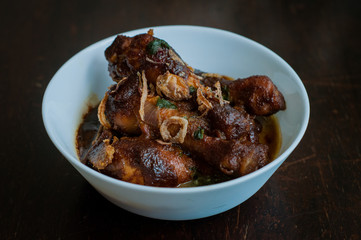 Malaysian dish of Ayam Masak Kicap or deep fried chicken in black soy gravy in a white bowl.