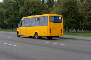 Fototapeta premium The bus driver carries passengers along the route on a summer day. Yellow bus rides on the city highway. Back view