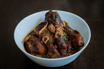 Malaysian dish of Ayam Masak Kicap or deep fried chicken in black soy gravy in a white bowl.