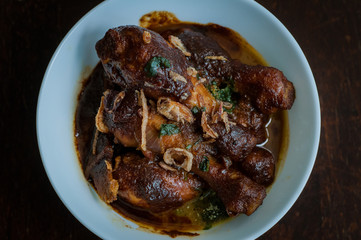 Malaysian dish of Ayam Masak Kicap or deep fried chicken in black soy gravy in a white bowl.