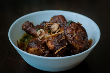 Malaysian dish of Ayam Masak Kicap or deep fried chicken in black soy gravy in a white bowl.
