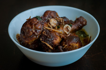 Malaysian dish of Ayam Masak Kicap or deep fried chicken in black soy gravy in a white bowl.