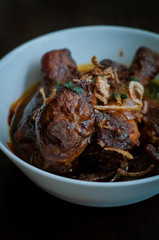 Malaysian dish of Ayam Masak Kicap or deep fried chicken in black soy gravy in a white bowl.