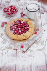 Homemade fruit pie (galette) made with fresh raspberries with powdered sugar on wooden table. Open pie, raspberry tart. Summer berry dessert. Empty space for text, copyspace.