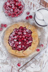 Homemade fruit pie (galette) made with fresh raspberries with powdered sugar on wooden table. Open pie, raspberry tart. Summer berry dessert. Flat lay.