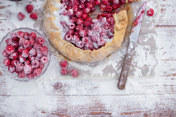 Homemade fruit pie (galette) made with fresh raspberries with powdered sugar on wooden table. Open pie, raspberry tart. Summer berry dessert. Flat lay. Empty space for text, copyspace.