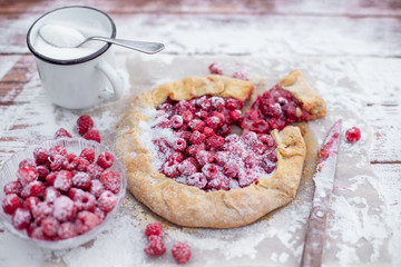 Homemade fruit pie (galette) made with fresh raspberries with powdered sugar on wooden table. Open pie, raspberry tart. Summer berry dessert. Flat lay