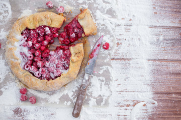 Homemade fruit pie (galette) made with fresh raspberries with powdered sugar on wooden table. Open pie, raspberry tart. Summer berry dessert. Flat lay. Empty space for text, copyspace.