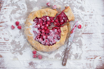 Homemade fruit pie (galette) made with fresh raspberries with powdered sugar on wooden table. Open pie, raspberry tart. Summer berry dessert. Flat lay