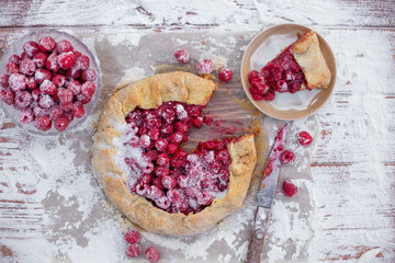 Homemade fruit pie (galette) made with fresh raspberries with powdered sugar on wooden table. Open pie, raspberry tart. Summer berry dessert. Flat lay