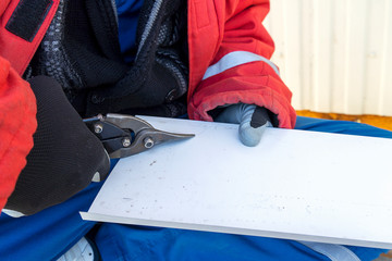 Builder scissors cuts a steel sheet. Worker tin cuts out the iron roof.