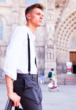 young European guy in shirt and trousers with suspenders walking around city
