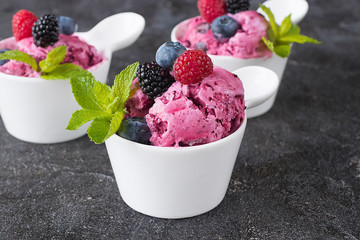 Three white cups with homemade popsicles made from fresh berries on a black background.