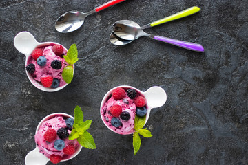 Three white cups with homemade popsicles made from fresh berries on a black background. Top view.