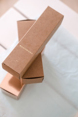 Set of three long package boxes in brown craft and rose gold color paper. Overhead, on white. Beauty, fashion blogging, minimalism concept