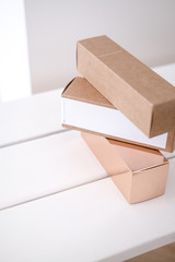 Set of three long package boxes in brown craft and rose gold color paper. On white. Beauty, fashion blogging, minimalism concept
