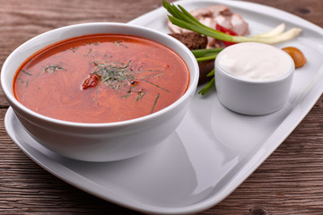 Ukrainian borsch with sour cream, onions and bacon on a white plate