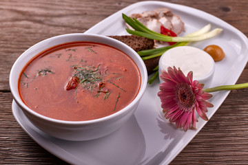Ukrainian borsch with sour cream, onions and bacon on a white plate
