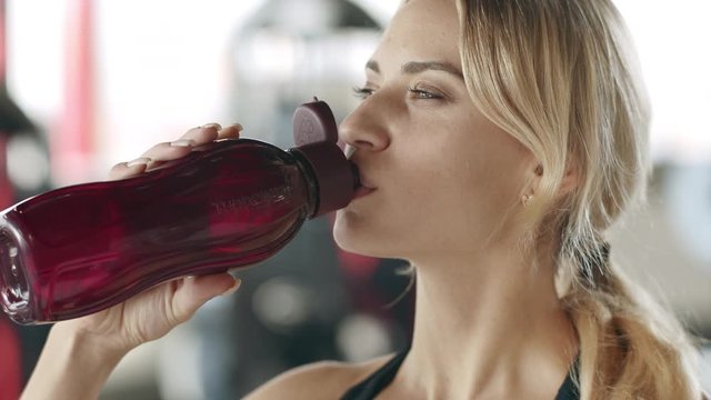Smiling sport woman drinking water in fitness gym. Happy girl sipping water