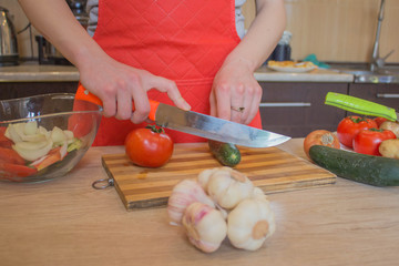 Young woman cooking healthy meal in the kitchen. Cooking healthy food at home. Woman in kitchen preparing vegetables. Chef cuts the vegetables into a meal