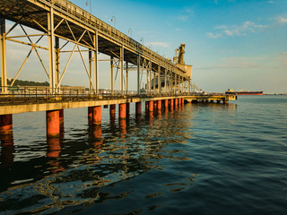 Fototapeta premium A dry cargo pier on a clear sunny day on stilts stands in the water of the sea with small waves.