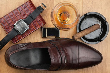Men accessories. Brown elegant shoes, wallet, alcohol and cigar on wooden table.