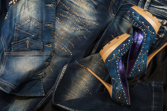 Luxurious women's denim shoes in rhinestones and jeans in rhinestones on a black silk. Fashion background.