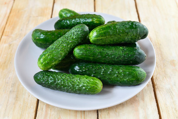 Fresh ripe ground cucumbers on a white plate isolated on a natural wooden table