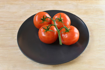 Fresh four ripe tomatoes  on black plate isolated on natural wooden table