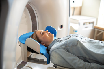 Joyful young woman lying on CT scanner table at radiology clinic - obrazy, fototapety, plakaty