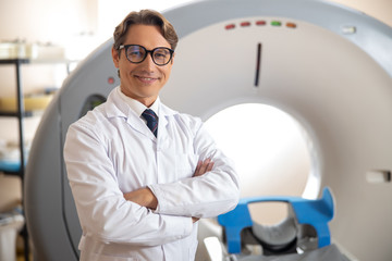 Fototapeta premium Joyful physician in glasses standing in scanner room at hospital
