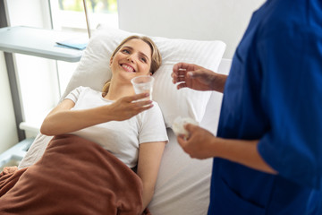 Obraz premium Smiling lady holding cup of water and looking at doctor