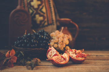 Detox snacking fruit. Vintage rustic still life. Fresh ripe pomegranate fruits with autumn leaves grapes on wooden background. Organic, healthy fruits.Toned image. Selective focus.