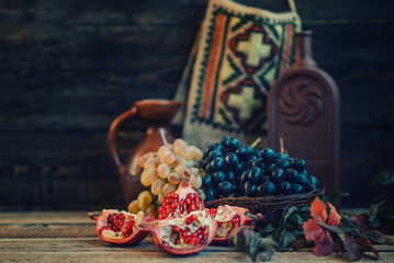 Organic ripe pomegranate fruit and grapes on wooden vintage background. Autumn harvest background. Vintage oriental still life. Toned image. Selective focus.