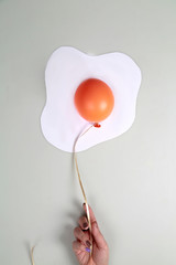 Orange balloon with white paper on grey background in shape of an egg. Food concept. Hand keep the balloon
