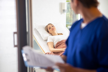 Fototapeta premium Young lady lying in bed and looking at doctor